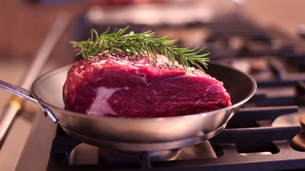 Rinderfilet mit Rosmarinzweig in einer Pfanne über offener Gasflamme