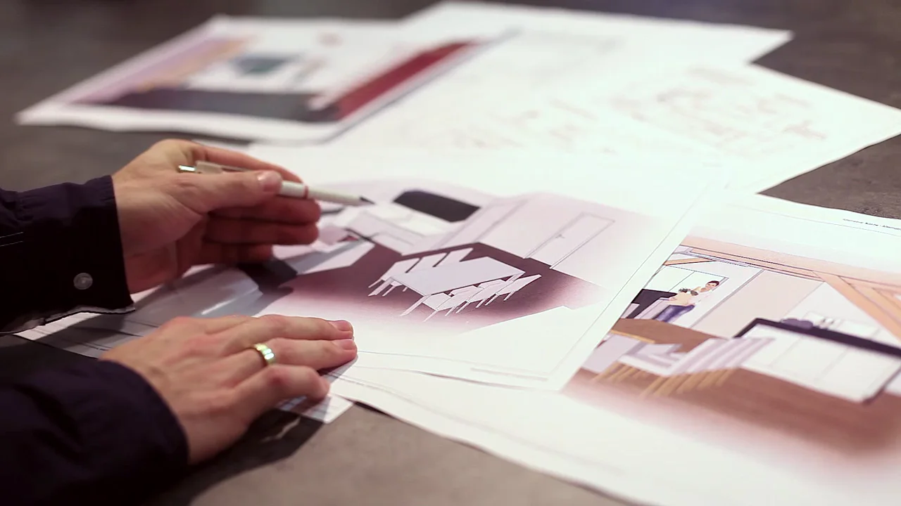 Hand mit Bleistift über ausgebreiteten Küchenzeichnungen auf einem Tisch