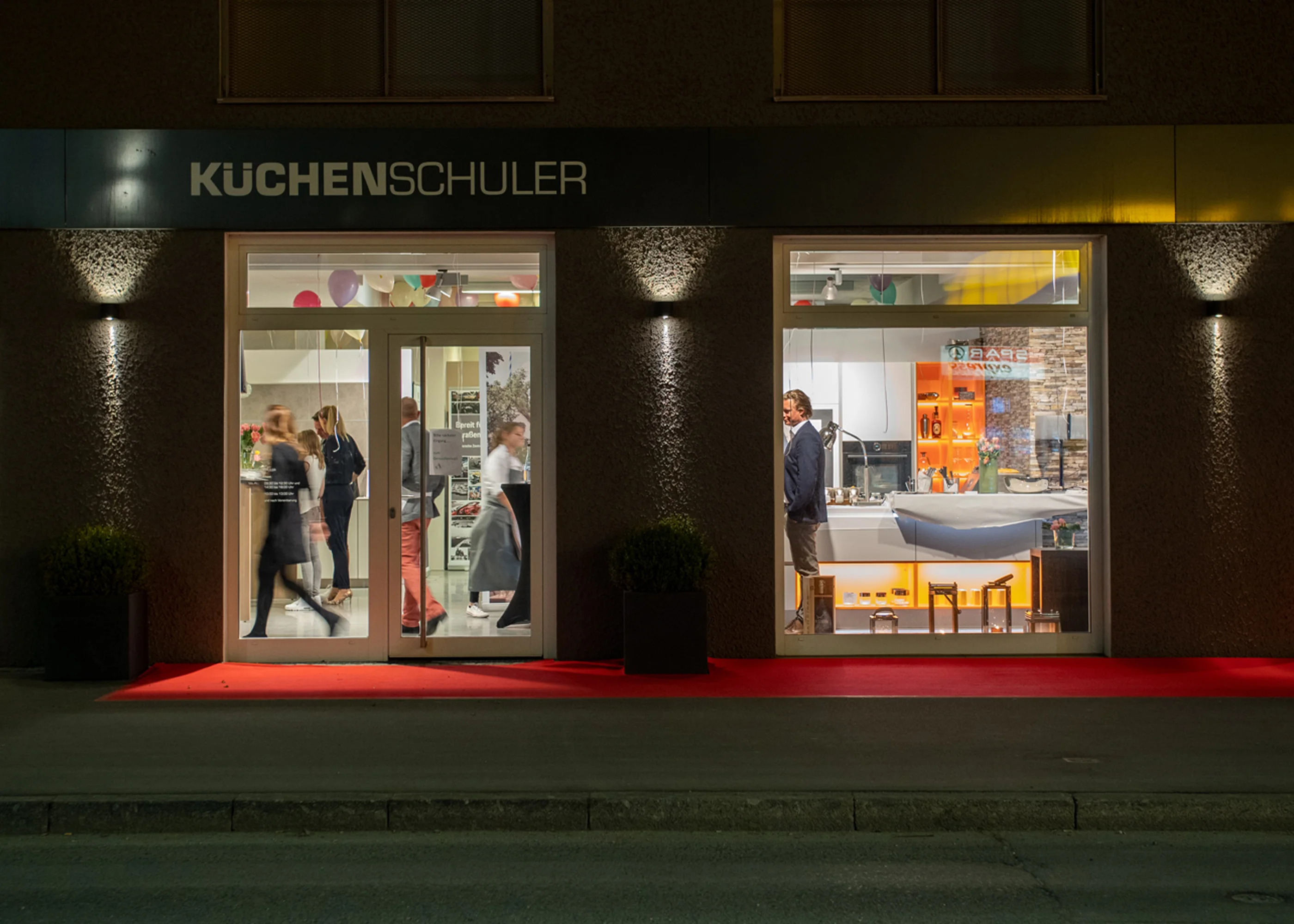 Das beleuchtete Ladengeschäft von Küchen Schuler am Abend, Blick von der Straße